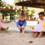 trois filles bien habillees jouent dans le bac a sable