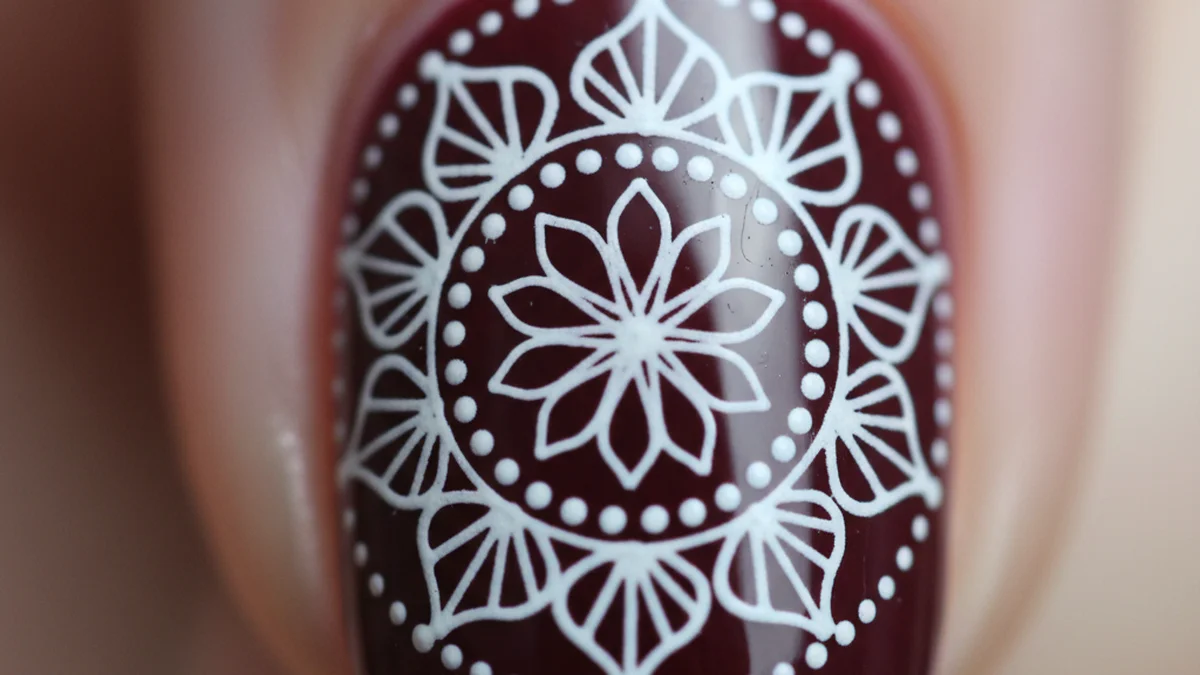 Motif mandala détaillé en blanc sur ongle bordeaux